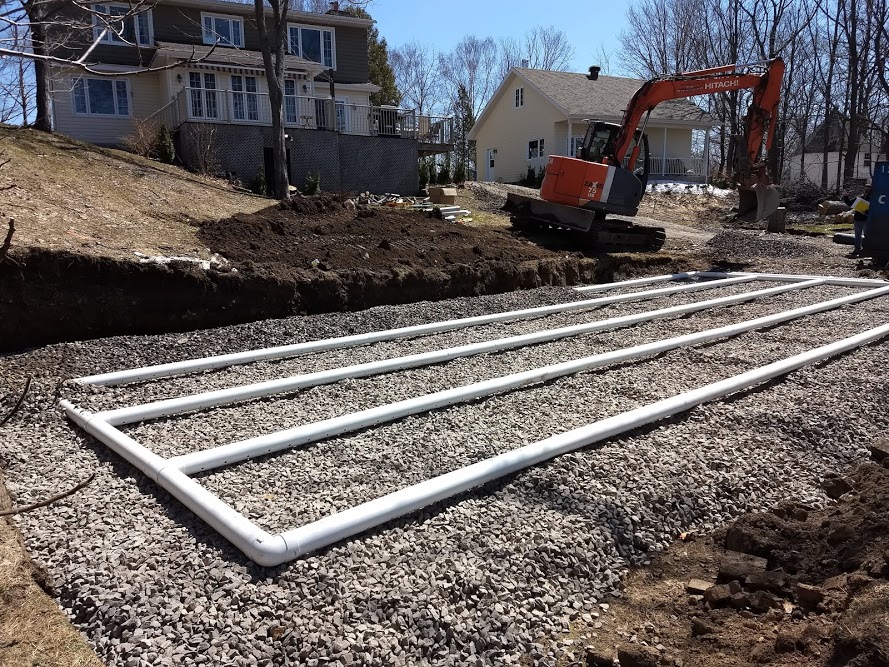 Residential septic drain field with perforated pipe grid on gravel and excavator